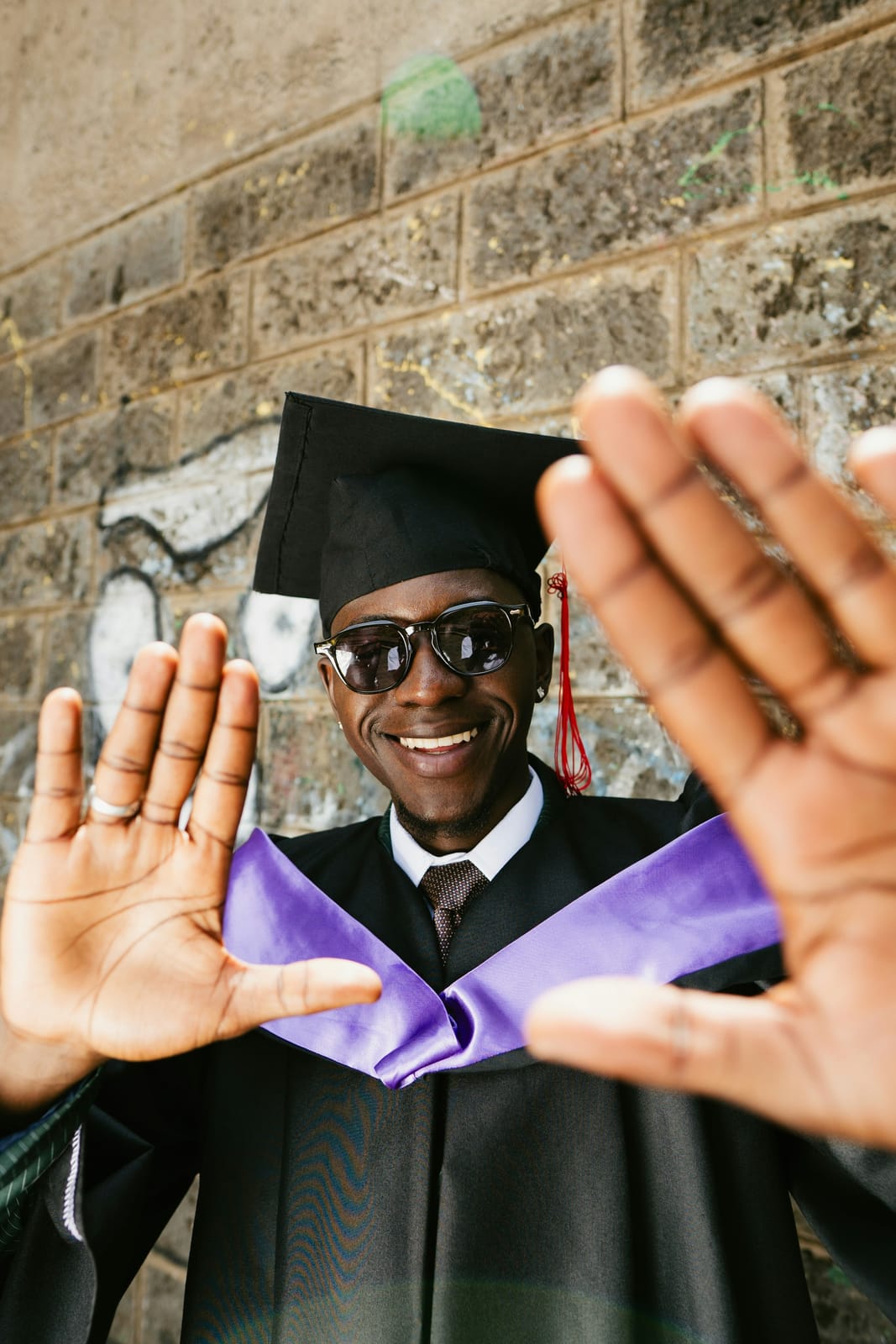 A smiling graduate in cap and gown, hands up.