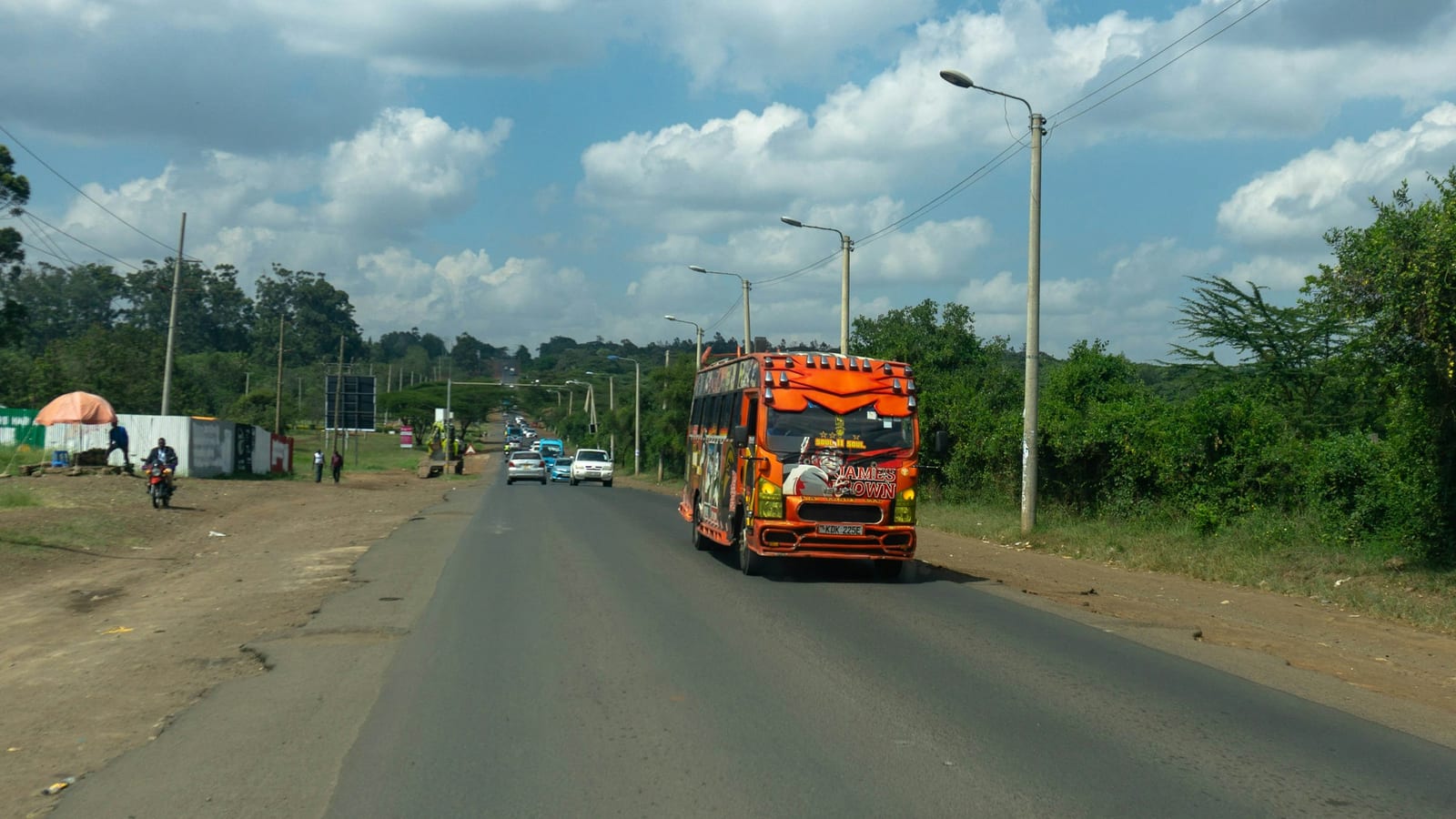 A brightly painted matatu driving along a Nairobi road under a big sky.
