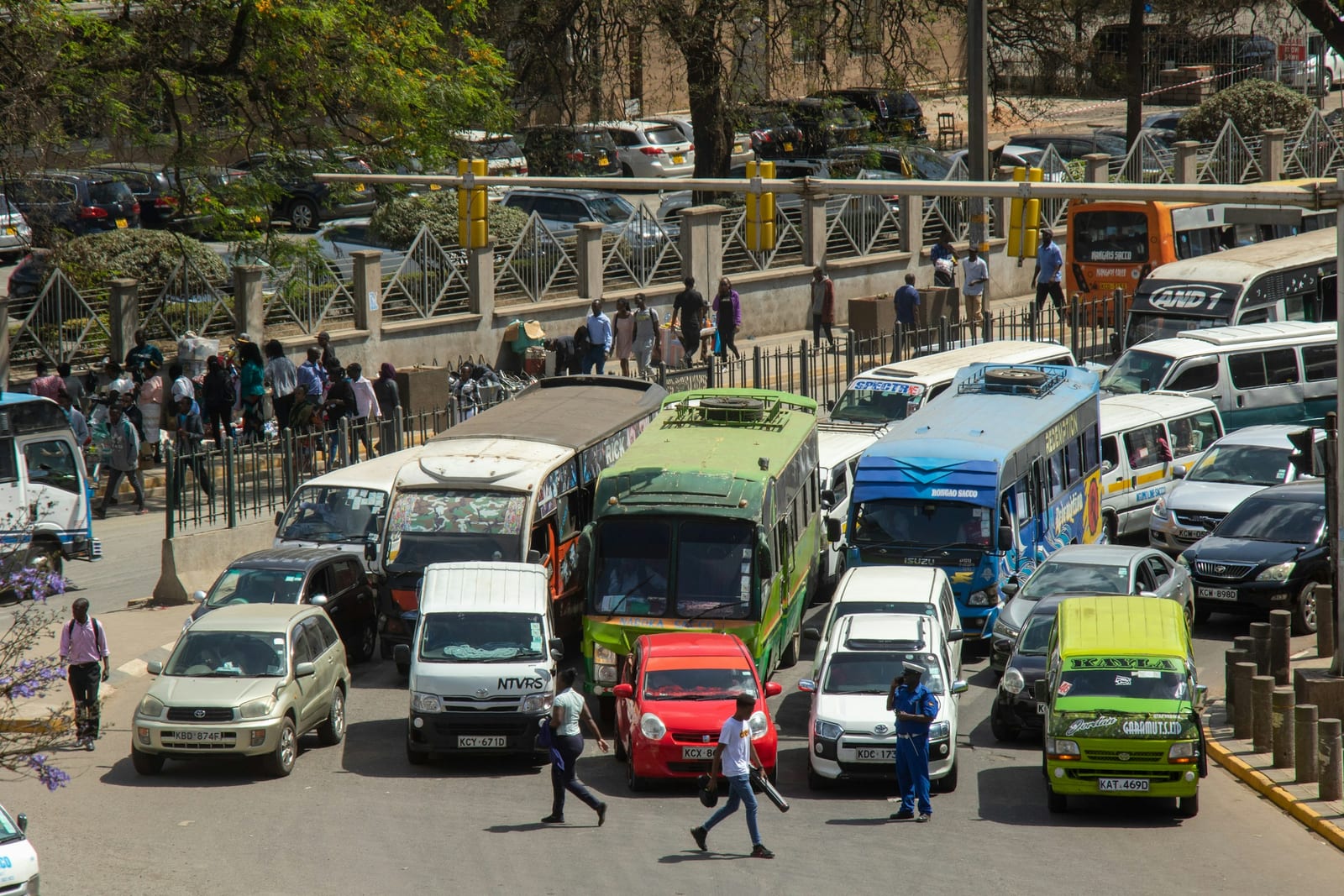 Matatus, buses and cars in a Nairobi traffic jam, people crossing between them.