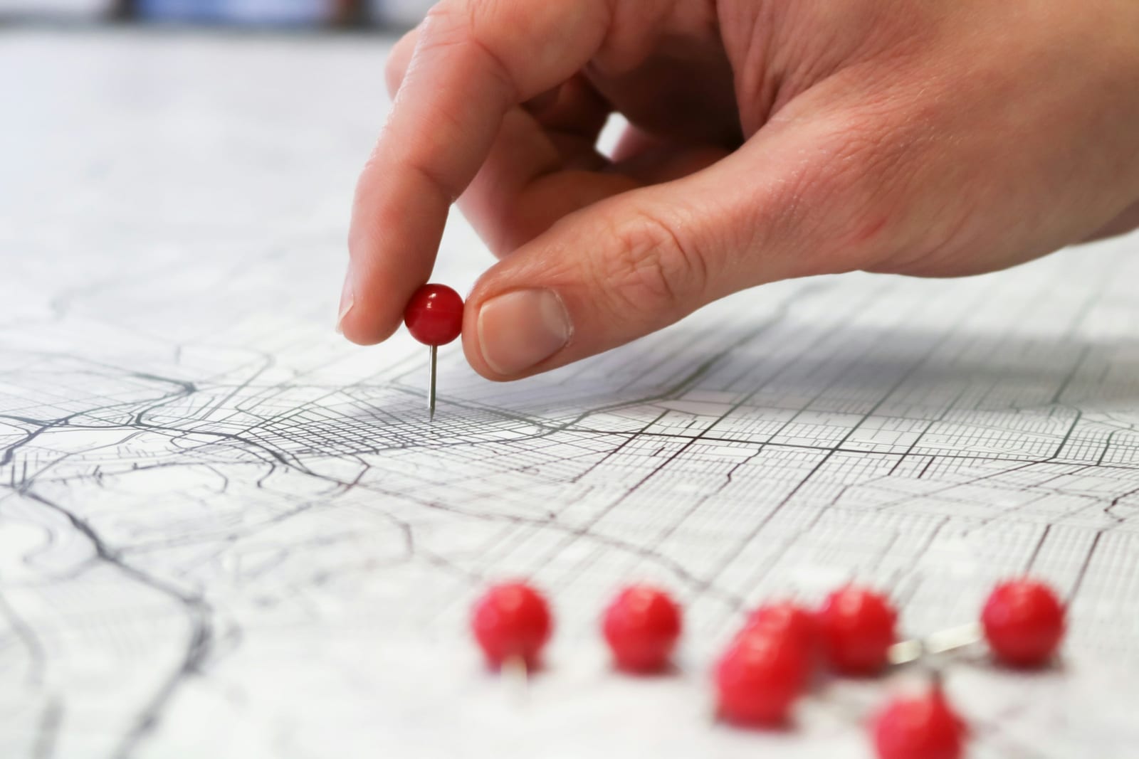 A hand pressing red pins into a printed city map.
