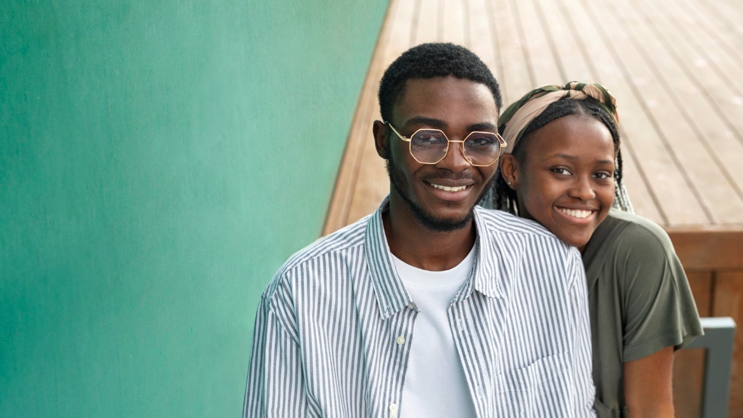 Two friends smiling close together against a green wall.