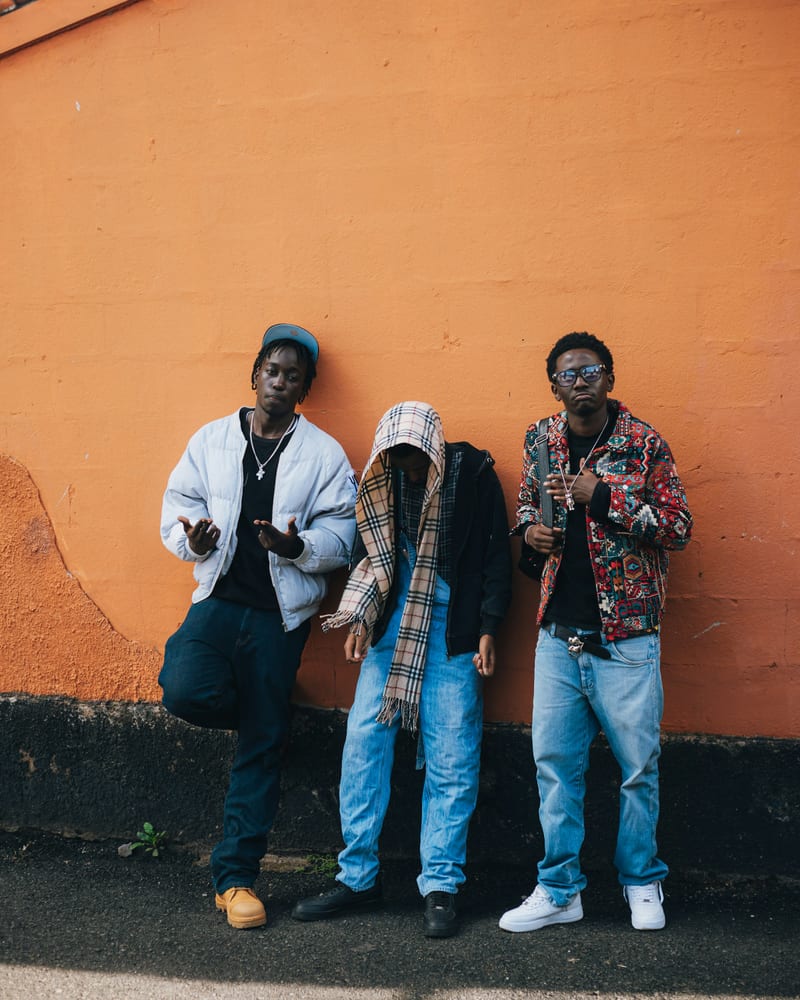 Three friends standing against a bright orange wall.