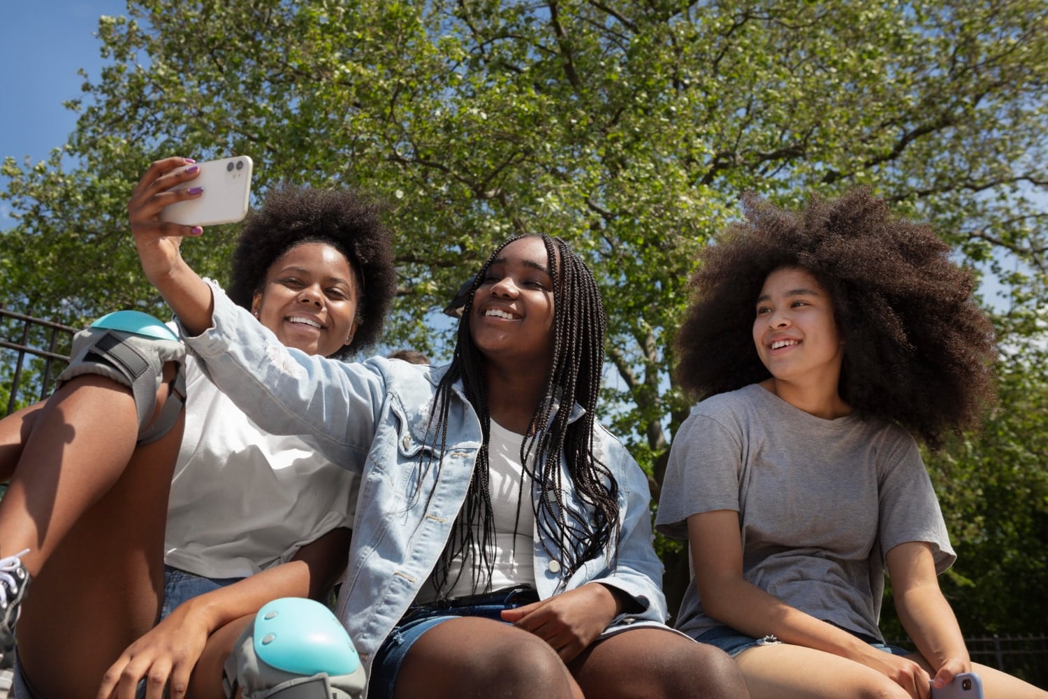 Three friends in a park take a selfie together, laughing in the sun.